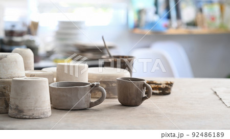 Handmade ceramic crockery, paint brushes, pottery shaping tools on wooden table in creative studio Handmade ceramic crockery, paint brushes, pottery shaping tools on wooden table in creative studio 92486189