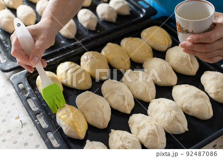 Woman brushing pies with beaten eggs before to put them in oven. Home baking. 92487086