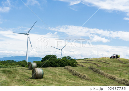 風車の見える夏空の下での牧草収穫の風景 92487786