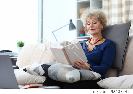 Elderly woman is reading book at home on couch 92488449