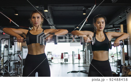 Two sporty girls do exercises with dumbbells in the gym. Two sporty girls do exercises with dumbbells in the gym. 92488458