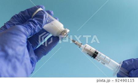 vaccination concept, in hands syringe and glass vial with medicine for injection close-up, blue background, 92490115