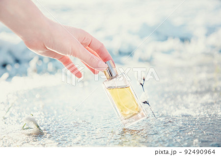 A woman's hand gracefully holds a rectangular transparent glass bottle of golden perfume on ice. Blurred background. Perfume and Fragrance template concept A woman's hand gracefully holds a rectangular transparent glass bottle of golden perfume on ice. Blurred background. Perfume and Fragrance template concept 92490964