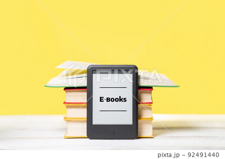 Knowledge. E-book reader and a stack of books on a yellow background. Copy space. Concept of education and electronic gadgets Knowledge. E-book reader and a stack of books on a yellow background. Copy space. Concept of education and electronic gadgets 92491440