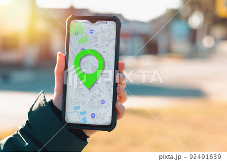A female's hand holds a cellphone with an open online maps app with marked place. The concept of online navigators and applications for smartphones 92491639