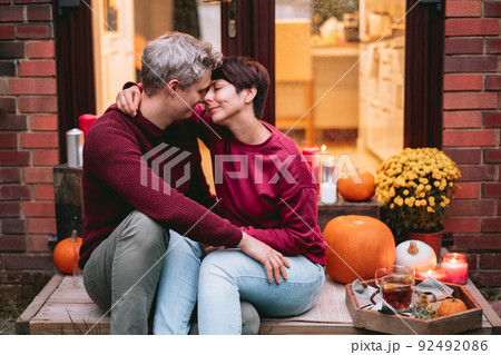 A couple having a romantic date on the porch of their home. Cozy ideas on how to spend time at home. Autumn tea time outdoors on house entrance decorated with pumpkins, flowers and burning candles 92492086