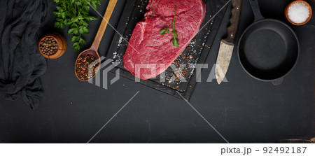 Raw beef tenderloin lies on a brown wooden board, black table. Raw beef tenderloin lies on a brown wooden board, black table. 92492187