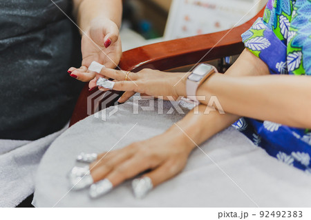 Woman in nail salon receiving a manicure by a beautician with cotton wool. 92492383
