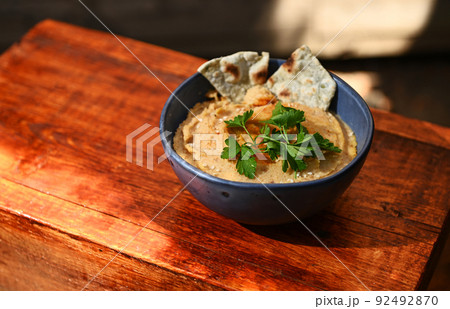 Chickpea hummus dip with pita bread on a blue ceramic bowl, above view on wooden background with copy ad space for text Chickpea hummus dip with pita bread on a blue ceramic bowl, above view on wooden background with copy ad space for text 92492870