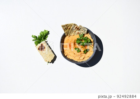 Flat lay. Blue ceramic bowl with chickpea hummus sprinkled with red chili and parsley wrapped in pita bread. Still life 92492884