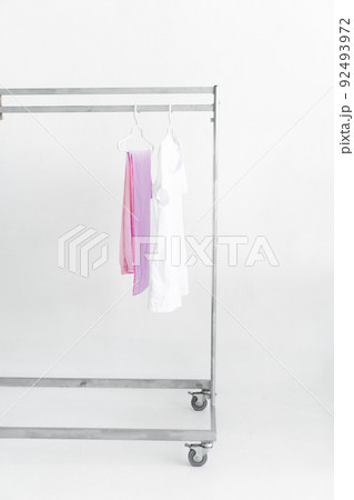 white medical doctor or physician lab coats with pink pants hanging on clothes mobile grey hangers with wheels, on white background. copy space, selected focus. Vertical picture. 92493972
