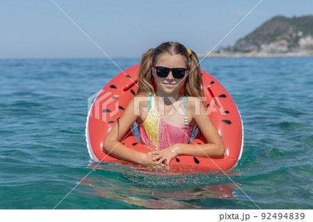 A young girl swims on an inflatable ring in the sea. 92494839