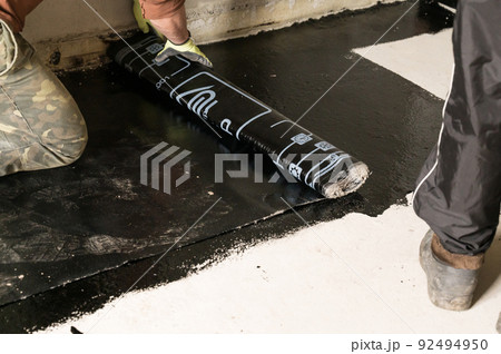 The worker untwists the roll of waterproofing and fastens it to the resin. 92494950