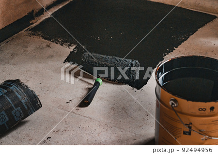Applying hot resin to the floor for waterproofing, roller and bucket of resin. 92494956