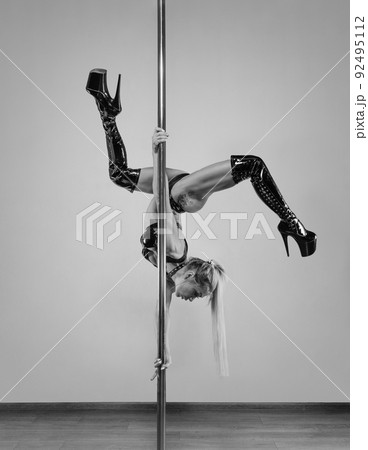 A female dancer is doing a Flag Back Roll or Butterfly move on a vertical pole. A female dancer is doing a Flag Back Roll or Butterfly move on a vertical pole. 92495112