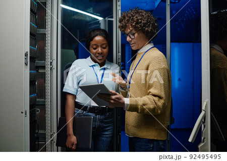 IT engineers standing beside server rack cabinet, doing wireless maintenance and diagnostics procedure with laptop IT engineers standing beside server rack cabinet, doing wireless maintenance and diagnostics procedure with laptop 92495495