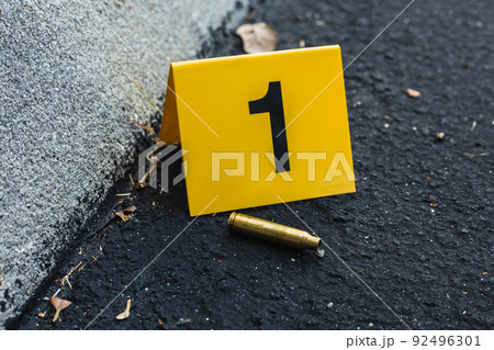 One yellow crime scene evidence marker on the street after a gun shooting brass bullet shell casing rifle 92496301