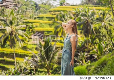 Beautiful young woman walk at typical Asian hillside with rice farming, mountain shape green cascade rice field terraces paddies. Ubud, Bali, Indonesia. Bali travel concept 92496423