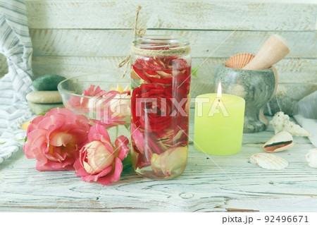 Fresh rose flowers and petal tincture, sea shells and stones, burning candles, on a wooden table, spa concept, natural cosmetics, body care, love emotion Fresh rose flowers and petal tincture, sea shells and stones, burning candles, on a wooden table, spa concept, natural cosmetics, body care, love emotion 92496671