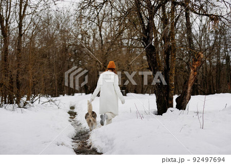 Happy young woman winter clothes walking the dog in the snow Lifestyle Happy young woman winter clothes walking the dog in the snow Lifestyle 92497694