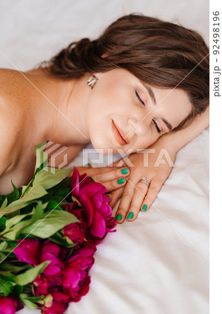 a gentle brunette woman in bed with a bouquet of peonies. morning of holiday. a gentle brunette woman in bed with a bouquet of peonies. morning of holiday. 92498196