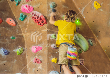 little boy climbing a rock wall in special boots. indoor little boy climbing a rock wall in special boots. indoor 92498473