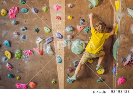 little boy climbing a rock wall in special boots. indoor 92498488