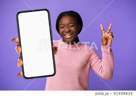 Joyful Black Young Woman Gesturing V-Sing And Showing Smartphone, Mockup 92498834