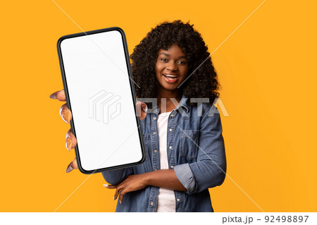 Happy beautiful black woman on yellow background, showing smartphone Happy beautiful black woman on yellow background, showing smartphone 92498897