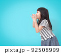 Cute little girl holding hands near mouth and making announcement, screaming on blue background with copy space. 92508999