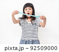 Cute girl 6 year old holding a blue slime and exited. Studio isolated on white background. 92509000