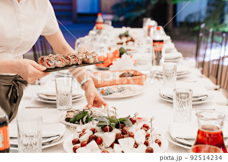 waiter puts on the table a black tray with baked Japanese rolls. 92514234