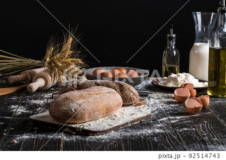 Beautiful still life with different kinds of bread, grain, flour on weight, ears of wheat, pitcher of milk and eggs 92514743