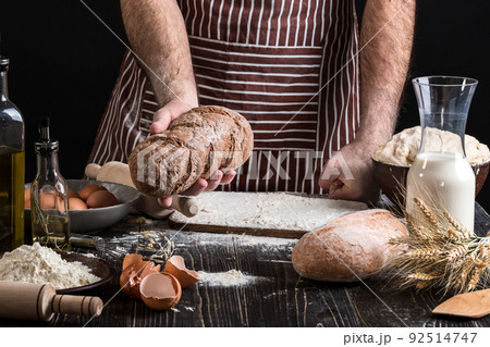 Chef holds the fresh bread in hand. Man preparing dough at table in kitchen. 92514747