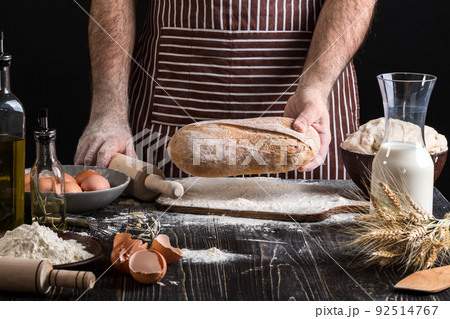 Chef holds the fresh bread in hand. Man preparing dough at table in kitchen. 92514767