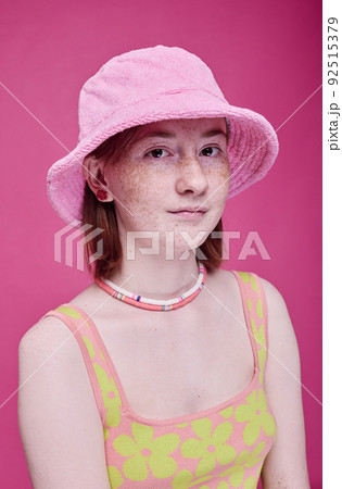Portrait of teenage girl with freckles in pink panama hat looking at camera against pink background Portrait of teenage girl with freckles in pink panama hat looking at camera against pink background 92515379
