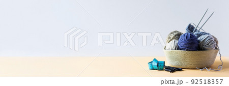 Gray and blue balls of thread in a beige basket with knitting needles for knitting warm clothes with scissors and a centimeter, knitting banner Gray and blue balls of thread in a beige basket with knitting needles for knitting warm clothes with scissors and a centimeter, knitting banner 92518357