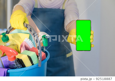 homeowner in rubber gloves holding detergent bottles. Hold mobile phone with blank empty green screen homeowner in rubber gloves holding detergent bottles. Hold mobile phone with blank empty green screen 92518887