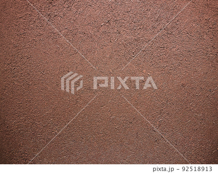 暗い赤茶色の土壁のなかに藁の粗い風合いが残る表面の横長の背景画像 92518913