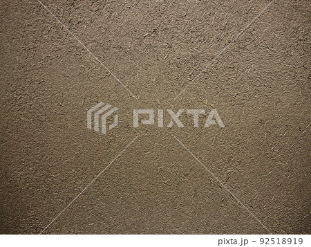 暗い薄茶色の土壁のなかに藁の粗い風合いが残る表面の横長の背景画像 92518919