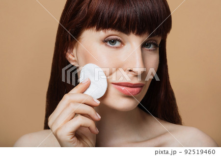 Beautiful red-haired woman, girl cleanses her skin with a cotton pad. 92519460