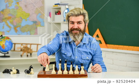 pieces and boards. happy school teacher. thinking of attacking and capturing opponent chess pieces. thinking of next move. bearded man training for chess competition. chess figures on wooden board 92520404
