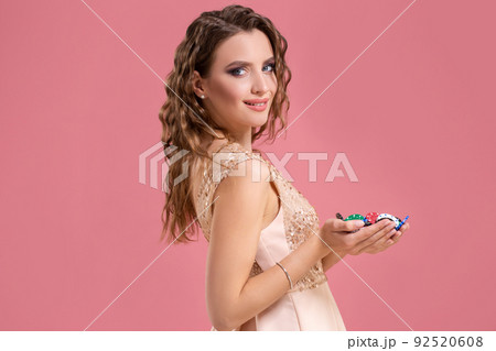 Young beautiful emotional woman with chips in hands on a pink background in the studio. Poker 92520608