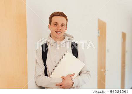 Smiling teenager leaning a wall in high school looking at camera 92521565