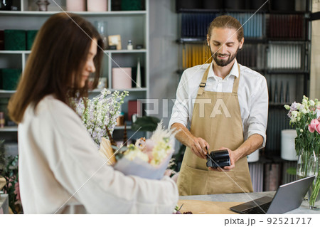 Attractive young man receives payment for a bouquet of flowers with credit card in flower shop 92521717