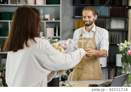 Hadsome bearded male florist receiving discount card from regular female customer Hadsome bearded male florist receiving discount card from regular female customer 92521718