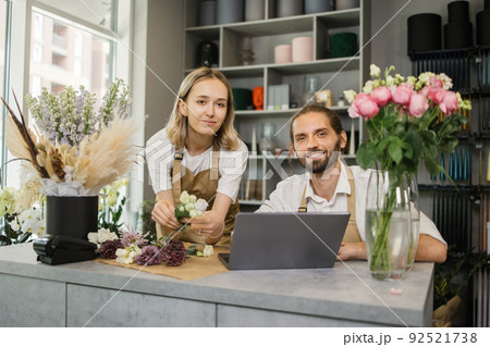 Two workers, man florist working on computer at workplace and woman helping him. Two workers, man florist working on computer at workplace and woman helping him. 92521738