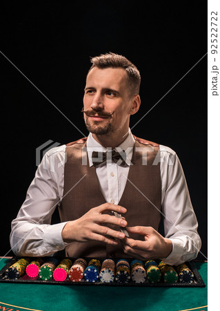 Portrait of a croupier is holding playing cards, gambling chips on table. Black background 92522722