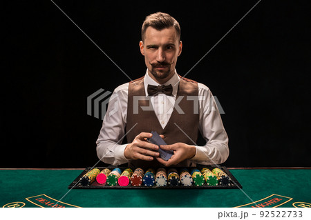 Portrait of a croupier is holding playing cards, gambling chips on table. Black background 92522733