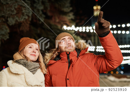 Horizontal shot of young couple walking on winter evening, man showing something to his girlfriend 92523910
